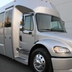 A silver bus is parked in front of a building.