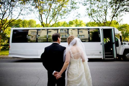 A bride and groom holding hands in front of a bus.