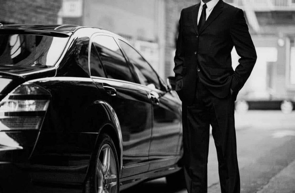 A man in suit and tie standing next to a car.